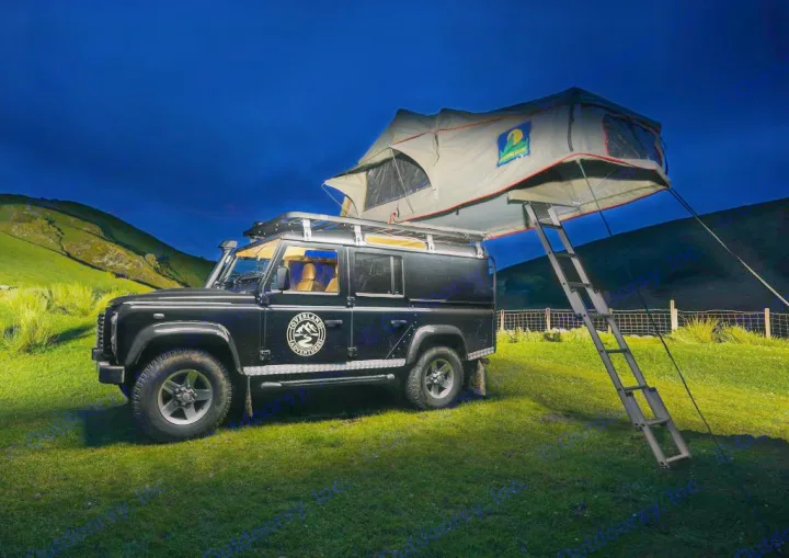 Black Land Rover Defender with rooftop tent deployed at night in a grassy field. An RV rental for rugged overland adventures.. Land Rover 2013 Land Rover Defender 110 XS Utility + 1 Roof Tent 2016