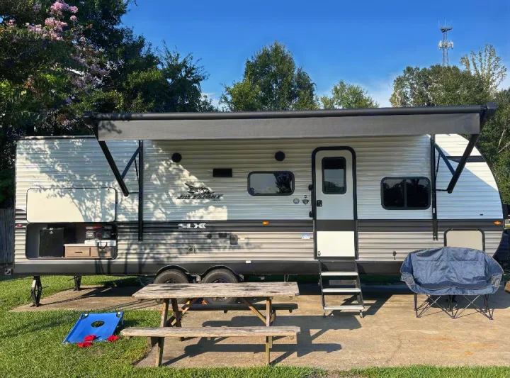 Your ideal rv rental setup: a Jay Flight travel trailer with outdoor kitchen, extended awning, picnic table, and cornhole game.. Jayco Jay Flight SLX 2024