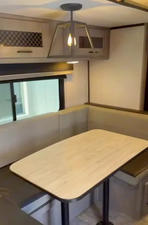 RV rental dinette with light wood-look table, booth seating, overhead cabinets, and stylish pendant light for dining.. Heartland RVs Mallard 2021