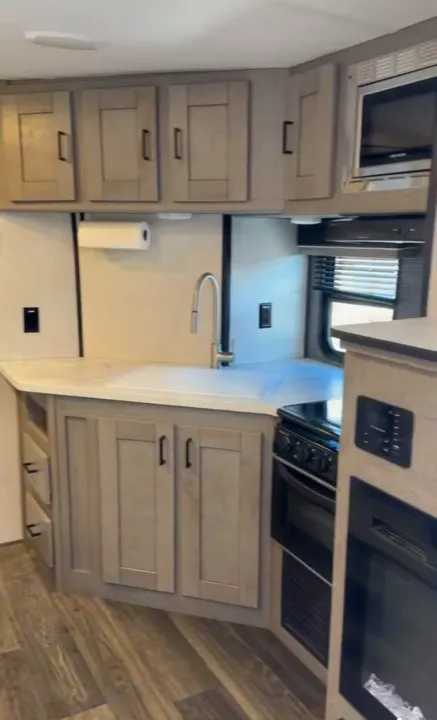 Compact RV rental kitchen with modern gray cabinets, white counters, sink, stove, and microwave. Wood-look flooring.. Heartland RVs Mallard 2021