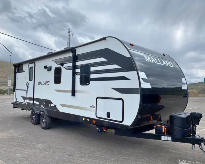 This sleek white and black Mallard travel trailer, perfect for an RV rental adventure, is parked on asphalt under a cloudy sky.. Heartland RVs Mallard 2021