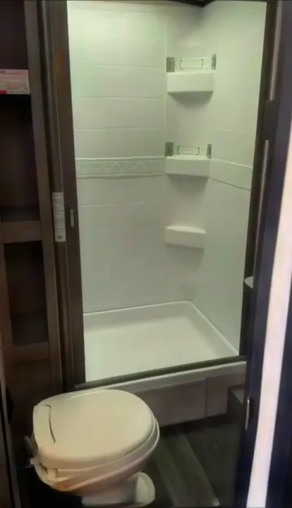 Functional RV rental bathroom with a white shower stall, built-in shelves, and a compact toilet.. Heartland RVs Mallard 2021