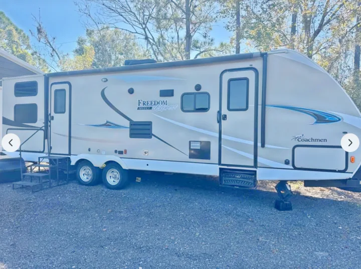Beige Coachmen Freedom Express RV rental travel trailer, with an awning and steps, parked on gravel.. Coachmen Freedom Select Express 28.7 2019