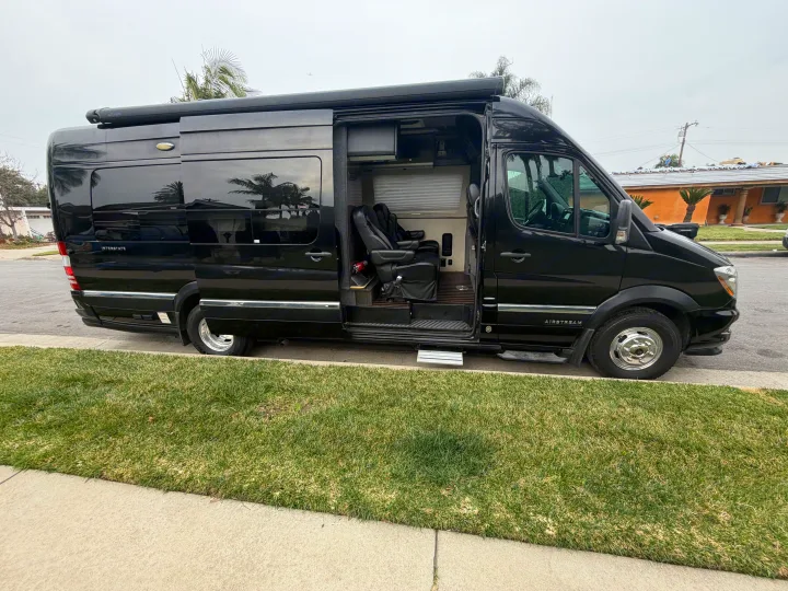 Black Airstream Interstate rv rental van, side door open revealing plush interior seats, parked street-side.. Airstream Interstate 2015