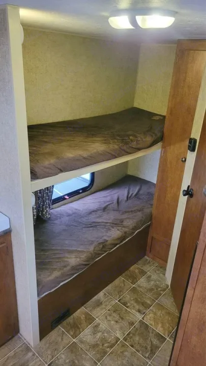 Interior view of an RV rental showing stacked bunk beds with dark bedding, a window, and patterned tile flooring.. Spree Escape 2016