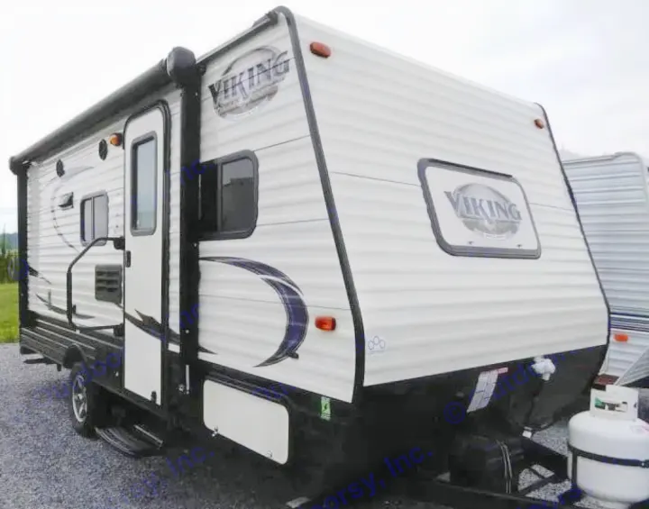 Viking travel trailer for rv rental. A white and black camper with awning and propane tank, parked on gravel.. Coachmen Viking 2017