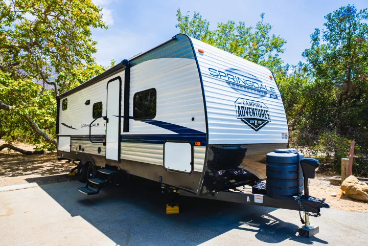 Experience the outdoors with this Springdale travel trailer rv rental, perfectly parked at a sunny campsite amidst lush trees.. Keystone Springdale 2024