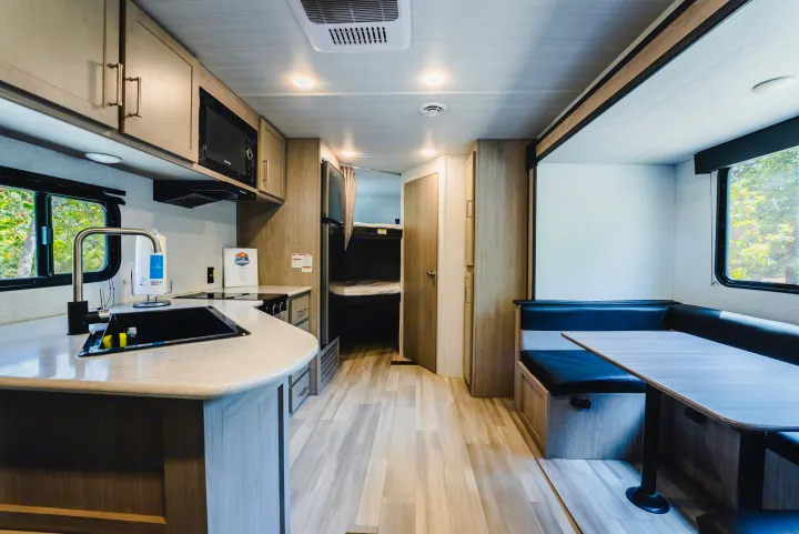 Inside a modern rv rental: kitchen with sink & microwave, dining booth, and bunk beds. Bright, spacious travel interior.. Keystone Springdale 2024