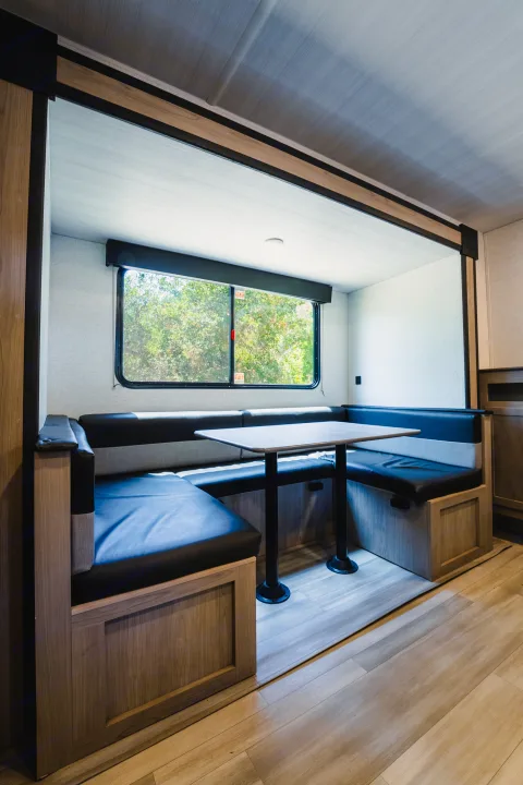 RV rental dinette: comfortable black booth seating, a table, and a large window with green trees for your travel adventures.. Keystone Springdale 2024