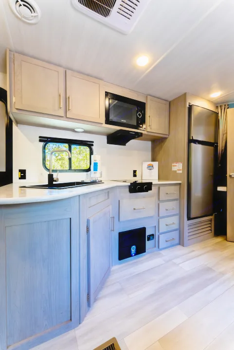 Modern RV rental kitchen featuring light wooden cabinetry, a sleek black sink, microwave, large fridge, and contemporary flooring.. Keystone Springdale 2024