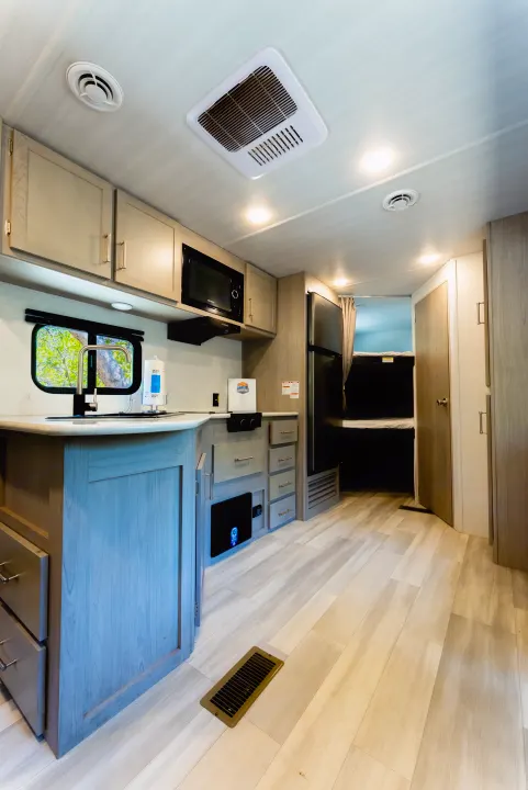 This RV rental features a modern kitchen with light wood-look cabinets, microwave, fridge, and sink, leading to a bunk area.. Keystone Springdale 2024