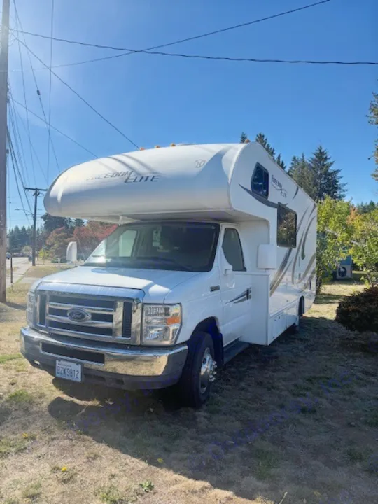Bright white Freedom Elite Class C rv rental, a motorhome parked on a grassy lawn under a sunny blue sky, awaiting adventure.. Thor Freedom Elite 2015