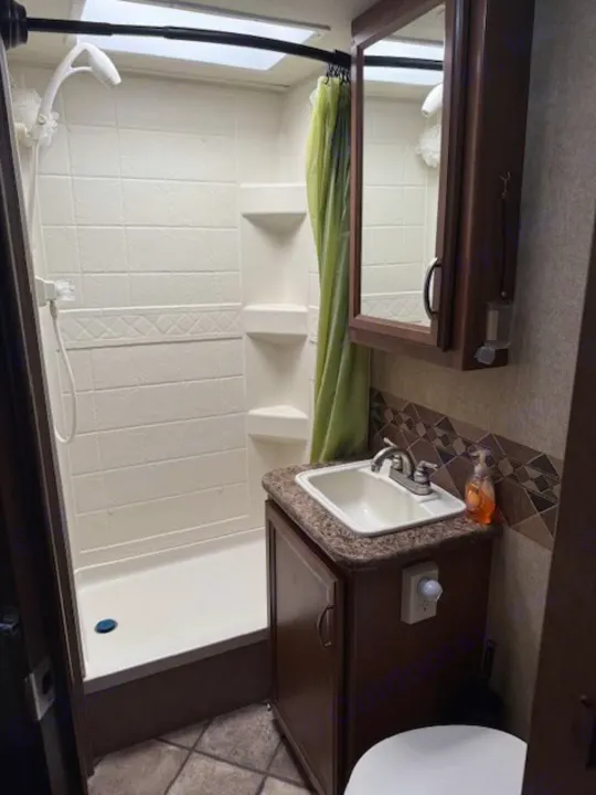 Compact and practical RV rental bathroom featuring a shower with skylight, sink vanity, and toilet.. Thor Freedom Elite 2015
