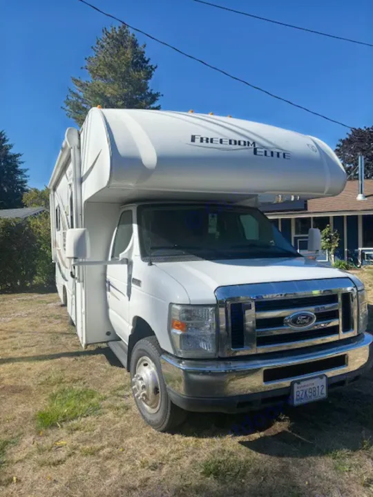 White Freedom Elite Class C RV rental parked on grass. Front-facing view with blue sky & Washington license plate BZX9812.. Thor Freedom Elite 2015