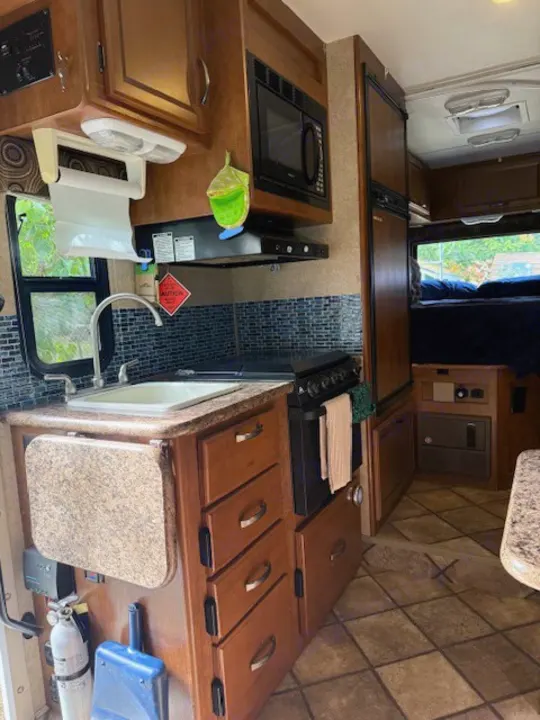 RV rental interior: A well-appointed kitchen featuring a sink, stove, microwave, and fridge. A sleeping area is visible behind.. Thor Freedom Elite 2015