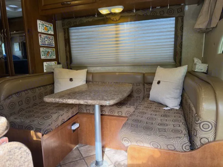 This RV rental shows a dinette with patterned booth seating, a granite-look table, and window blinds.. Thor Freedom Elite 2015