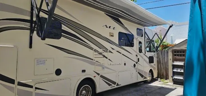 Discover adventure in this spacious beige RV rental, featuring graphic decals and an extended awning, parked outdoors.. Thor A.C.E. 2018