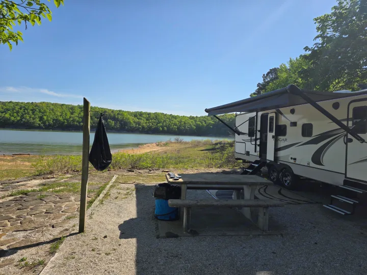 This RV rental, parked lakeside with an extended awning and picnic table, offers beautiful views of forests and water.. Keystone RV Cougar 2022