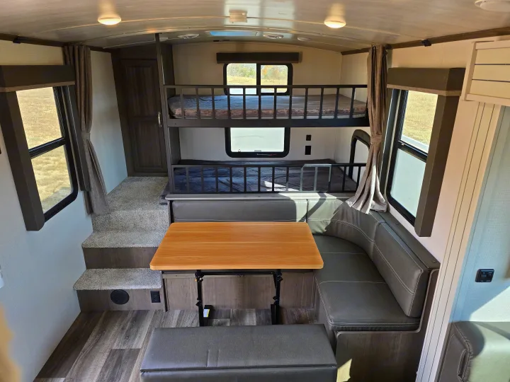 RV rental interior: cozy dinette, steps, and sturdy bunk beds. Bright windows offer views from this travel trailer.. Keystone RV Cougar 2022