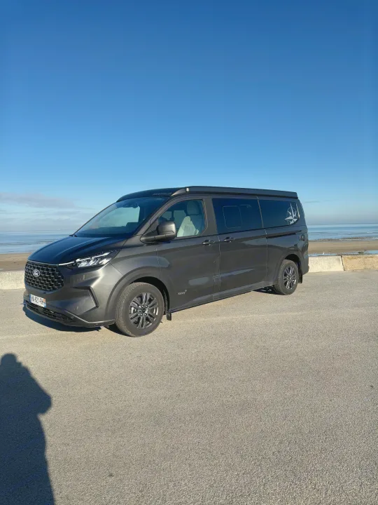 This sleek Ford Westfalia camper van, perfect for your next rv rental adventure, is parked by the sunny beach under a clear blue sky.. Westfalia Kelsey 2024