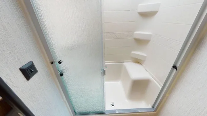 Compact shower-tub combo in an RV rental bathroom, featuring a textured sliding glass door & built-in shelves.. Forest River Palomino Solaire 2021
