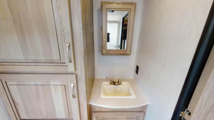RV rental bathroom with compact sink, mirrored cabinet, and light wood cabinetry.. Forest River Palomino Solaire 2021