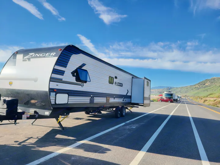 A Zinger travel trailer, a perfect RV rental option, is parked with its slide-out extended on a sunny day next to scenic hills.. Crossroads RV Zinger 2021