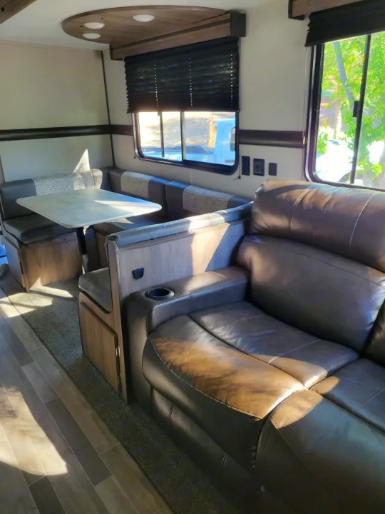 RV rental interior with a cozy dining booth and a comfortable reclining sofa featuring a built-in cup holder.. Crossroads RV Zinger 2021