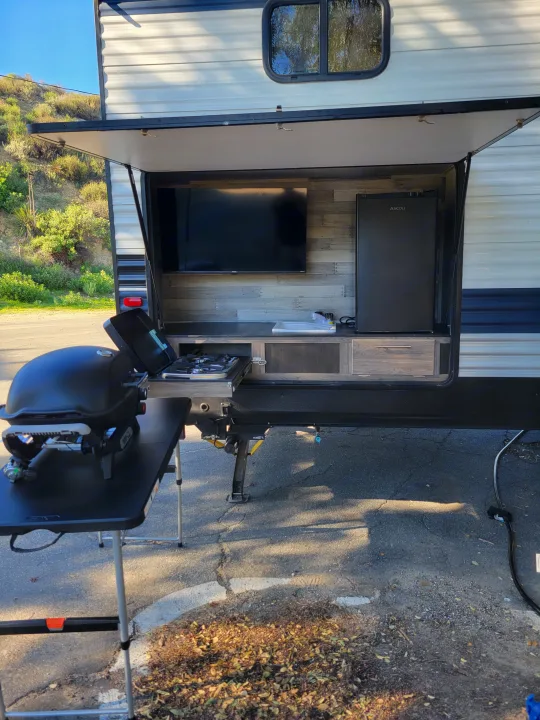 RV rental: Outdoor kitchen with TV, fridge, sink, stove, and a portable grill on a table.. Crossroads RV Zinger 2021