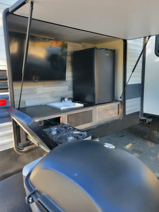 Outdoor RV rental kitchen: TV, fridge, sink, pull-out gas grill/cooktop. Ideal for camping convenience.. Crossroads RV Zinger 2021