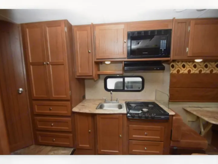 Inside an RV rental, showcasing a fully equipped kitchen with wood cabinetry, sink, stove, microwave, and dinette.. Forest River Coachmen Leprechaun 2017