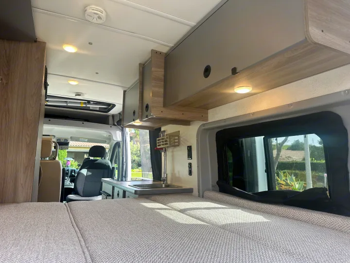Bright rv rental interior featuring a comfy bed, overhead storage, and a functional kitchenette, ready for adventure.. Winnebago Solis 2022