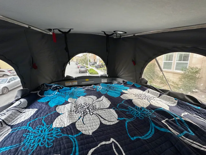 Cozy rv rental pop-top bed with a floral quilt and street views through arched windows from inside.. Winnebago Solis 2022