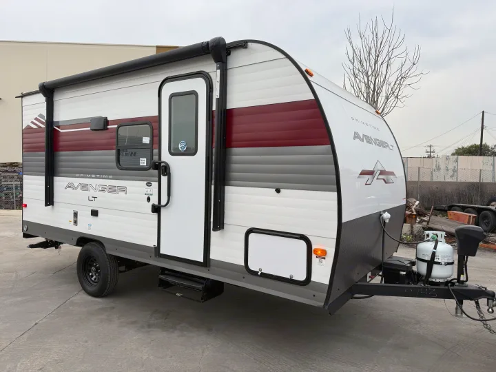 A compact white, red, and gray Primetime Avenger LT travel trailer, ideal for an rv rental, parked outdoors.. Forest River Avenger LT 2025