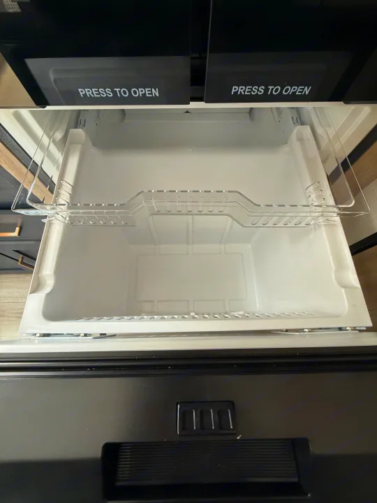 Inside an rv rental appliance: a clean, empty white pull-out drawer with a clear shelf, below two "PRESS TO OPEN" compartments.. Forest River Avenger LT 2025