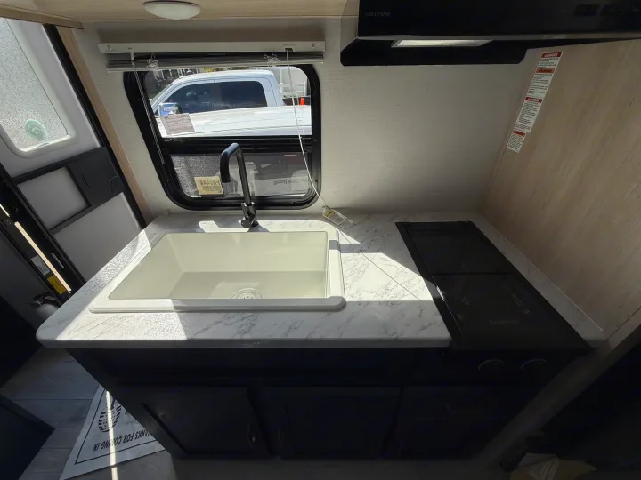 RV rental kitchen: white sink, black stovetop, Greystone range hood, and marble-style countertop, lit by a window.. Forest River Avenger LT 2025