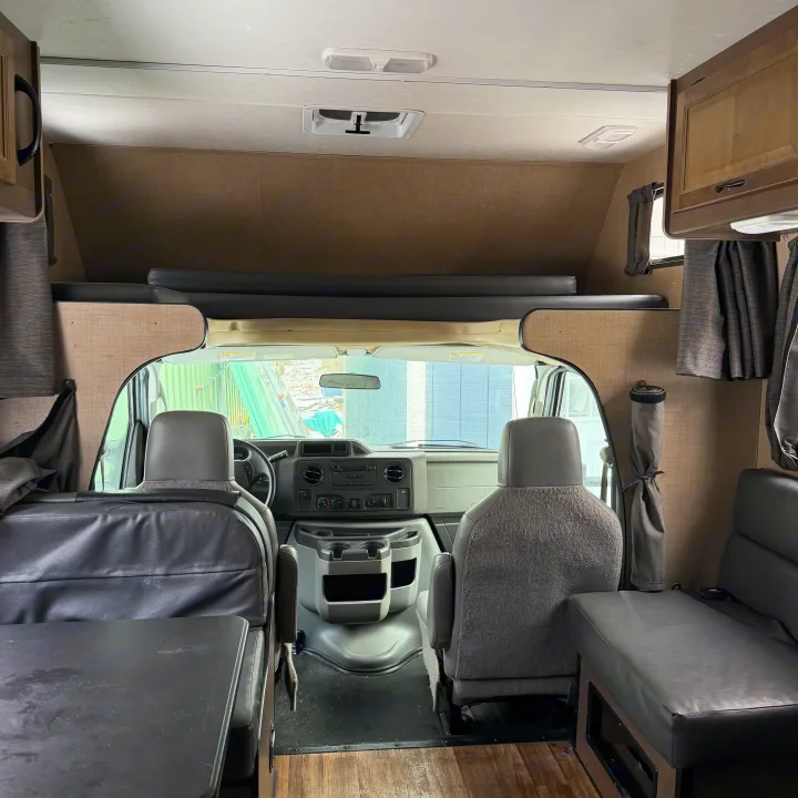 RV rental interior view: Looking towards the front, showing the cockpit with seats, dashboard, and an overhead sleeping bunk.. Thor Motor Coach Four Winds Majestic 2018