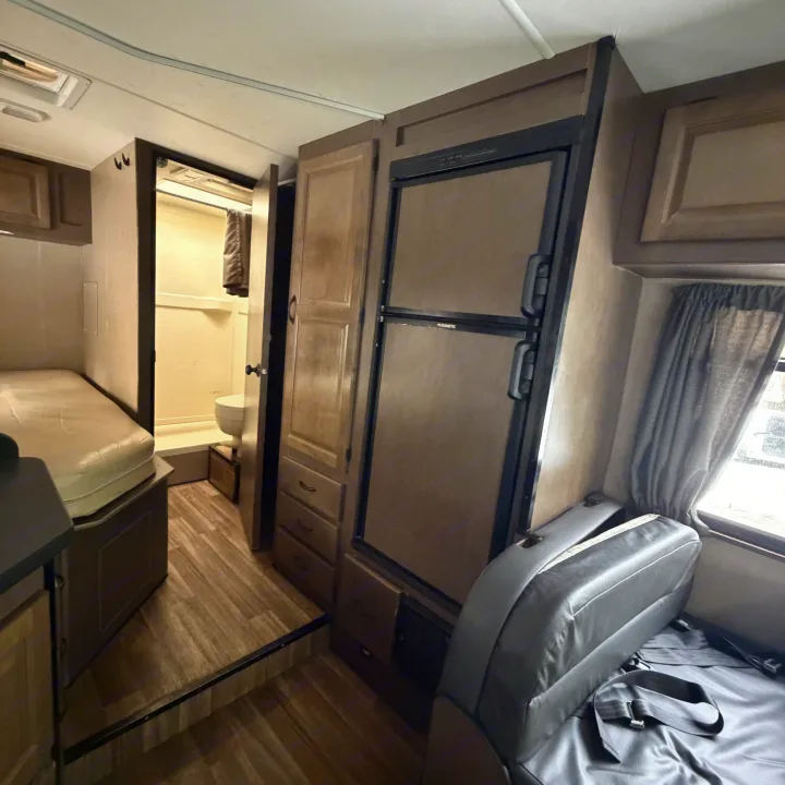 RV rental interior view showcasing a compact living area with refrigerator, wardrobe, bed, and bathroom, ideal for road trips.. Thor Motor Coach Four Winds Majestic 2018