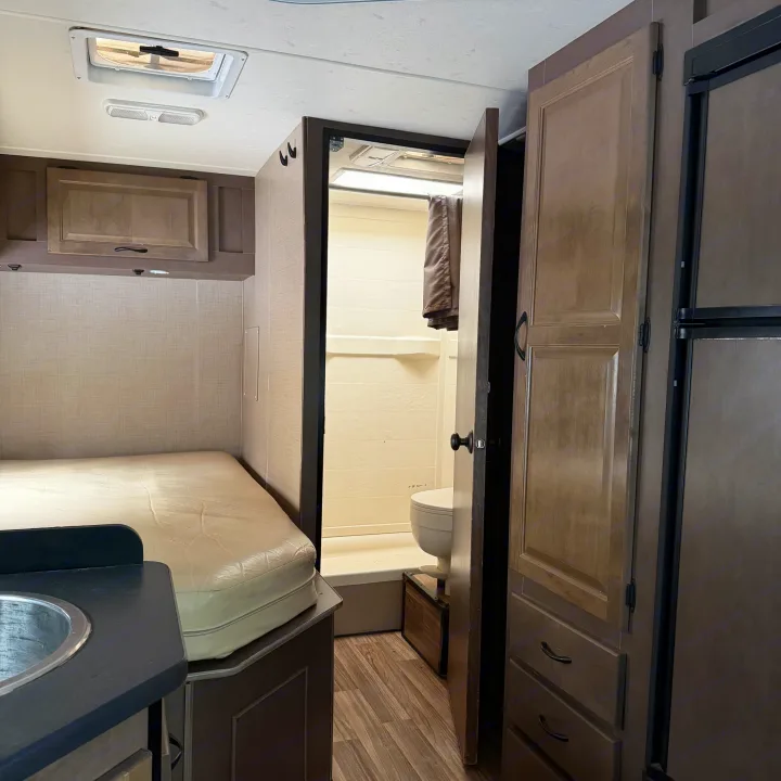 Compact RV rental interior showing a bed, small sink, and an open door to the bathroom with a toilet and shower.. Thor Motor Coach Four Winds Majestic 2018