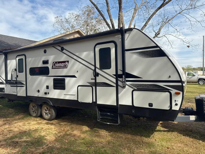 Modern white Coleman rv rental travel trailer, parked on grass. Features dual axles, entry steps, and awning rail for your adventure.. Dutchmen Coleman Light 2022