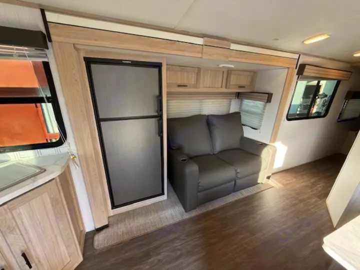 Modern rv rental interior with a Dometic refrigerator, gray reclining loveseat, compact kitchen, and wood flooring.. Cruiser RV Shadow Cruiser 248RKS 2022