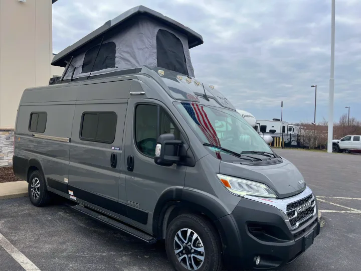 A gray Ram-based camper van with a raised pop-top roof, seen outdoors, ideal for an rv rental adventure.. Winnebago Solis 2025
