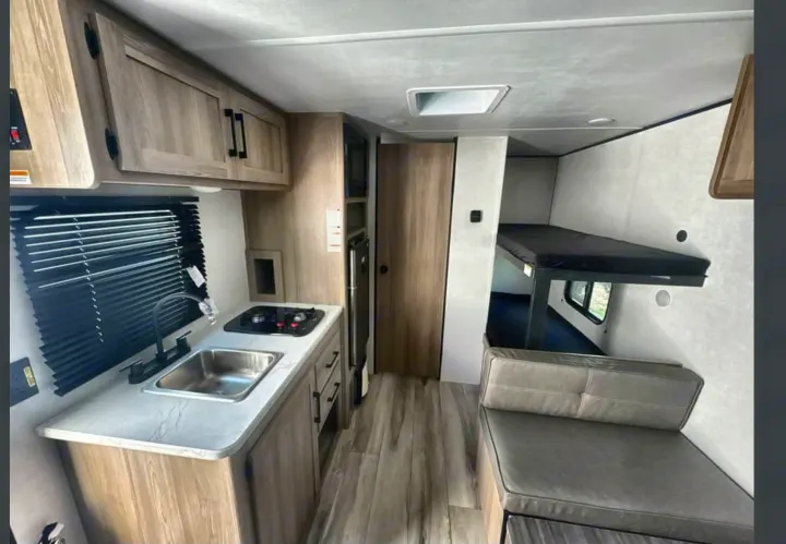 RV rental interior featuring a compact kitchen with sink and stove, upper cabinets, bunk beds, and a comfy seating area.. Heartland RVs Prowler 2022