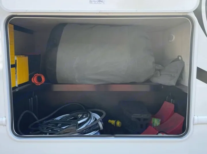 RV rental storage bay: power cords, leveling blocks, wheel chocks, and covered gear neatly stored.. Thor Freedom Elite 2026