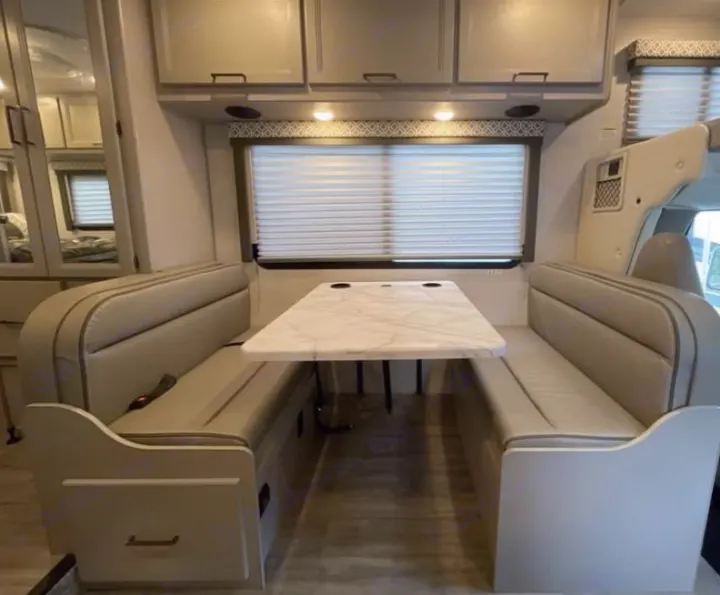 Spacious RV rental dinette area with comfortable bench seating, a marble-look table, and overhead cabinets for storage.. Thor Freedom Elite 2026