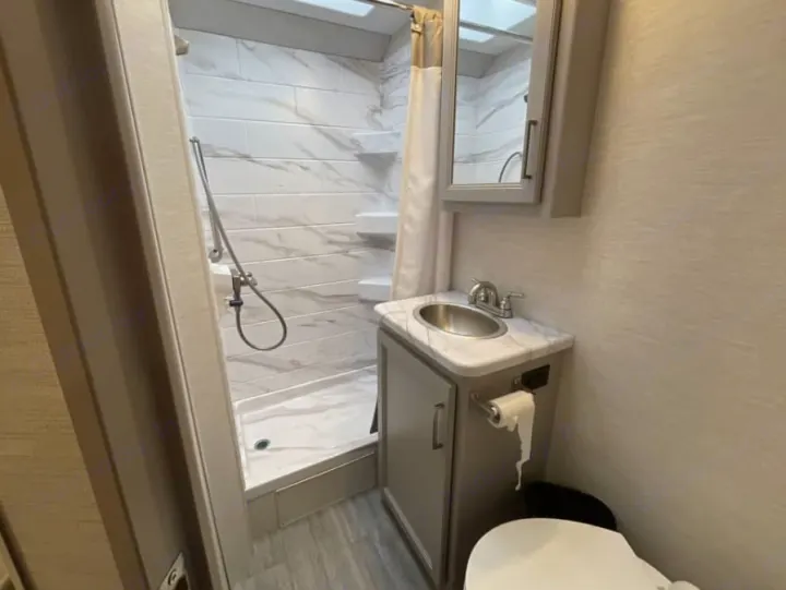 This clean RV rental bathroom has a tiled shower, sink, toilet, and mirrored cabinet, ideal for travel.. Thor Freedom Elite 2026