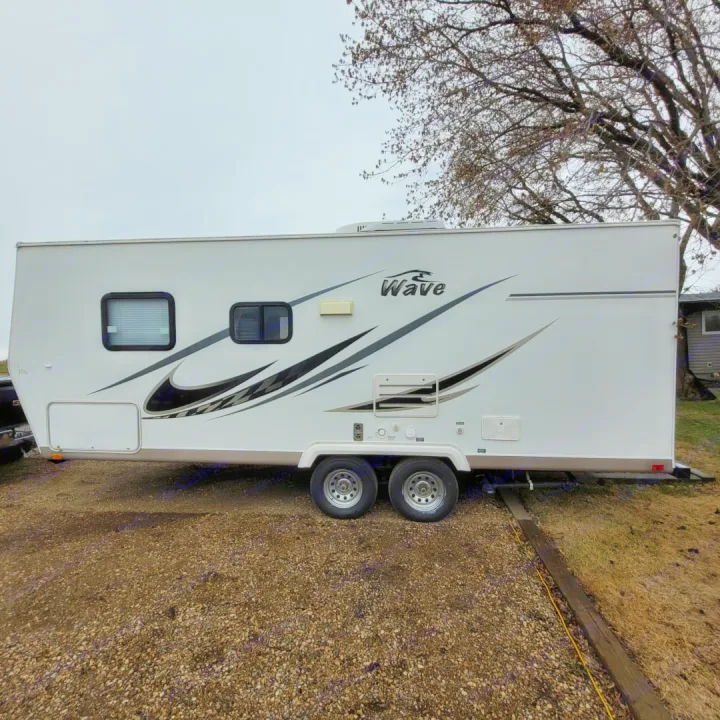 White "Wave" travel trailer with dual axles and modern graphics, parked on gravel. Consider this great rv rental option!. Thor Wave 2006