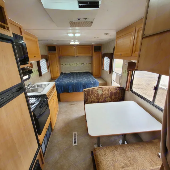 Spacious RV rental interior features a kitchen, bedroom with blue bedding, and a cozy dinette dining area.. Thor Wave 2006
