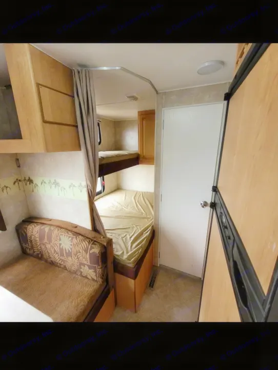 RV rental interior featuring cozy bunk beds with a privacy curtain, a patterned dinette, and a wood-paneled refrigerator.. Thor Wave 2006