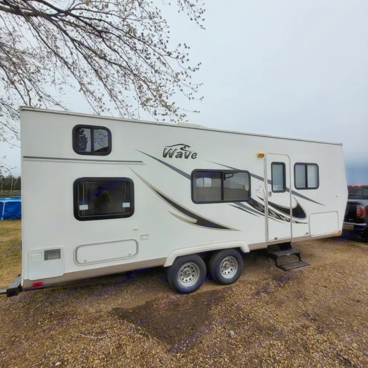 White "Wave" travel trailer, a great option for an RV rental, parked on gravel under a cloudy sky.. Thor Wave 2006